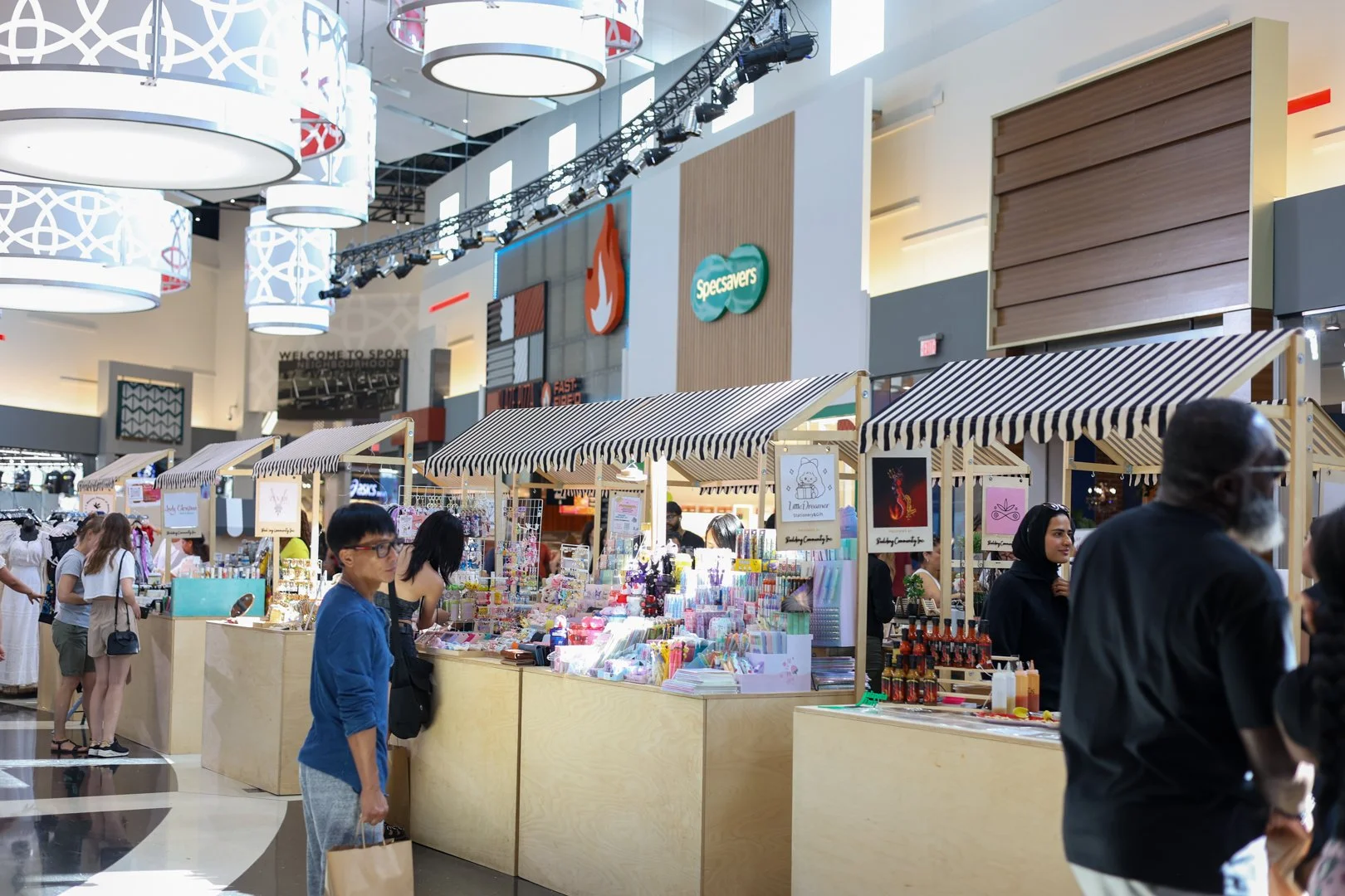 Shoppers browsing Building Community Inc. kiosks with striped awnings at Vaughan Mills